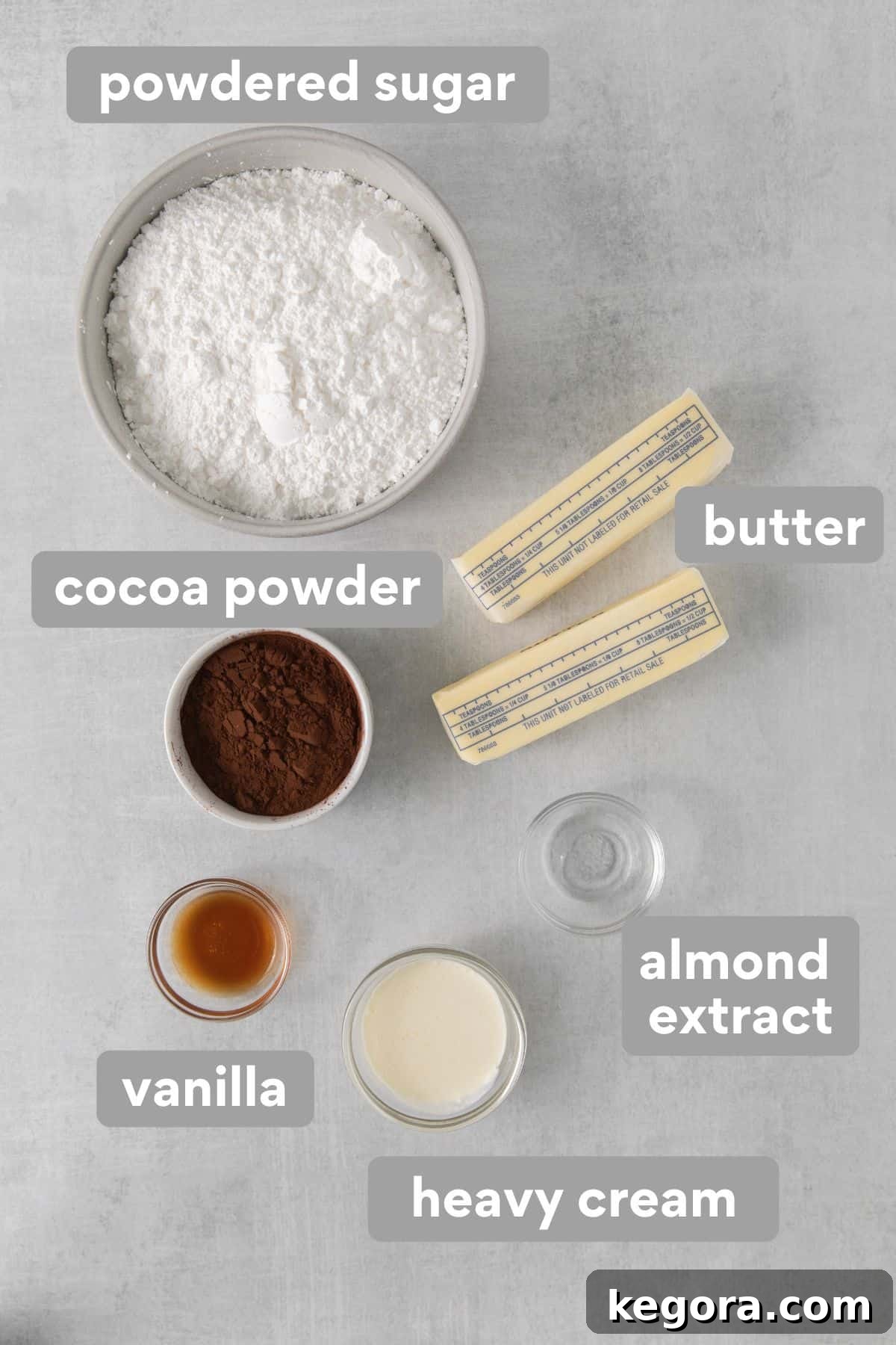 Decadent Gluten Free Chocolate Delights 5 Ingredients for gluten-free chocolate frosting, including butter, powdered sugar, cocoa powder, heavy cream, vanilla, and almond extract, neatly arranged on a countertop.