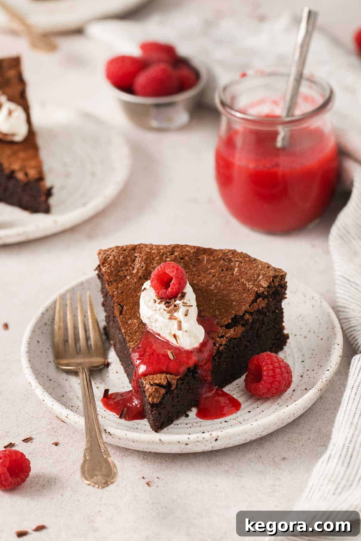 A luscious slice of flourless chocolate torte on a white plate, drizzled with vibrant raspberry sauce and garnished with fresh raspberries.