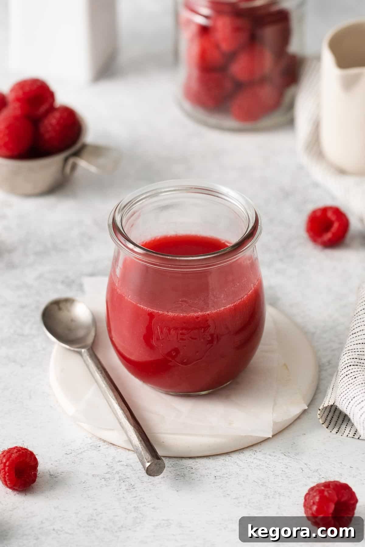 Vibrant Raspberry Drizzle 3 A beautiful glass jar filled with vibrant raspberry coulis, with a serving spoon resting beside it, ready to be enjoyed.