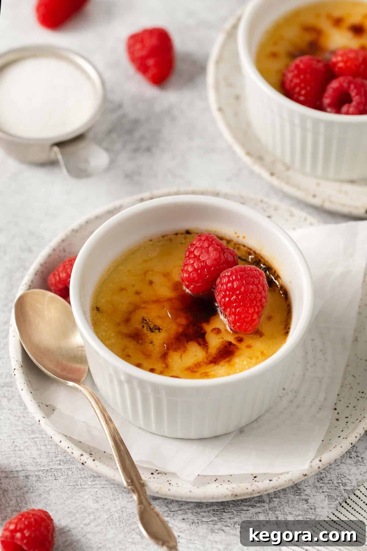 Dairy-Free Dream Brûlée 2 Dairy-free creme brulee in a ramekin, with vibrant raspberries on top and a spoon delicately placed on the side, ready to be enjoyed.