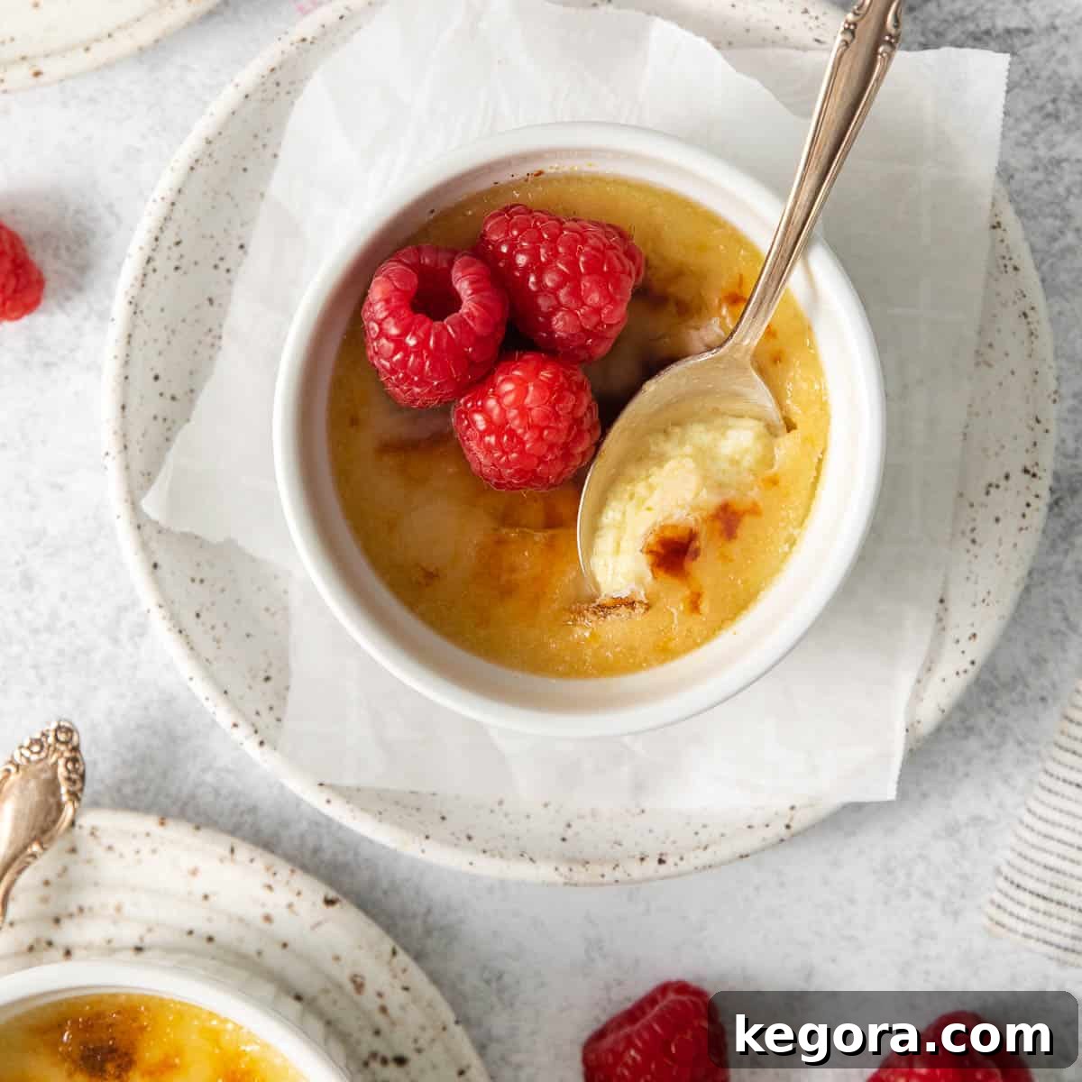 Dairy-Free Dream Brûlée 11 A dairy-free creme brulee in a ramekin, adorned with fresh raspberries, with a spoon gently dipping into the creamy custard, highlighting its luscious texture.