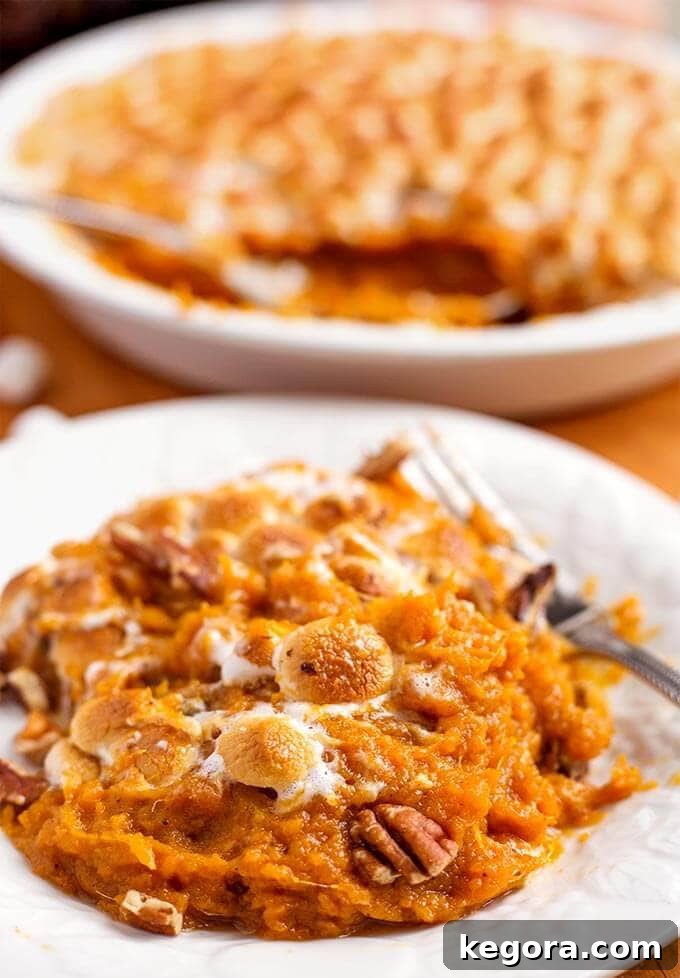 A close-up of Instant Pot Candied Yams on a white plate with a silver fork, showing the perfectly browned marshmallow topping.