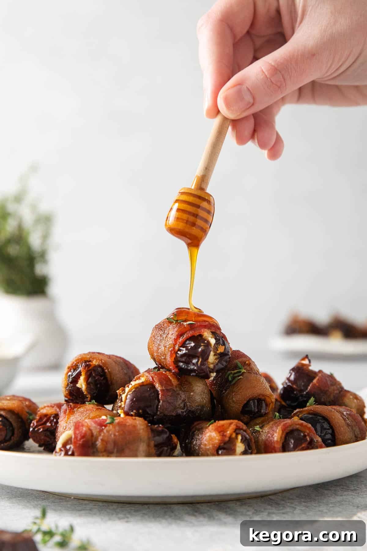 A hand drizzling hot honey over a plate of perfectly baked bacon-wrapped dates.