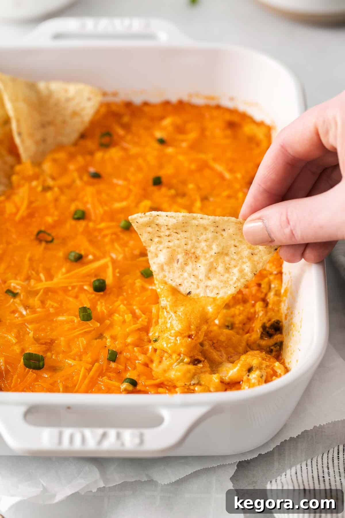 A hand holding a chip and dipping into the rich, creamy, and tangy dairy-free buffalo chicken dip, garnished with fresh green onions.