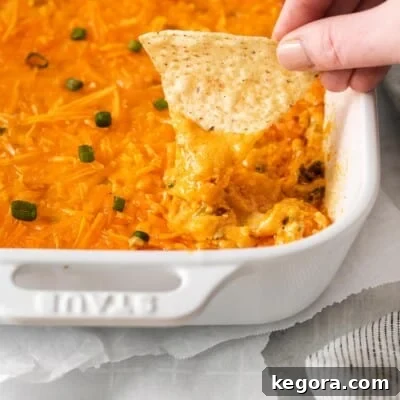 A close-up view of a hand dipping a chip into the warm and bubbly dairy-free buffalo chicken dip, highlighting its creamy texture and enticing color.