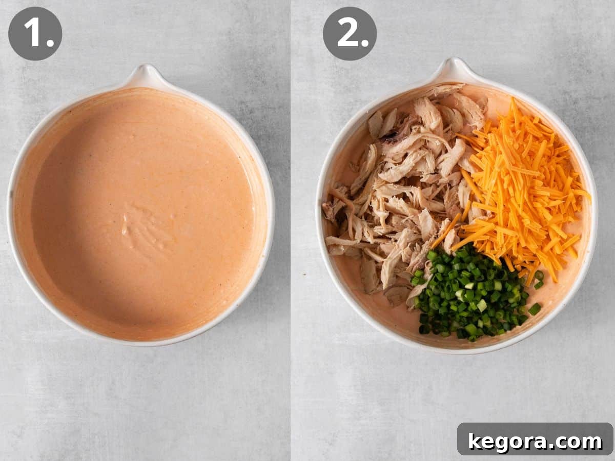 A mixing bowl filled with creamy dairy-free buffalo dip base, with separate piles of shredded chicken, dairy-free cheese, and sliced green onions ready to be stirred in.