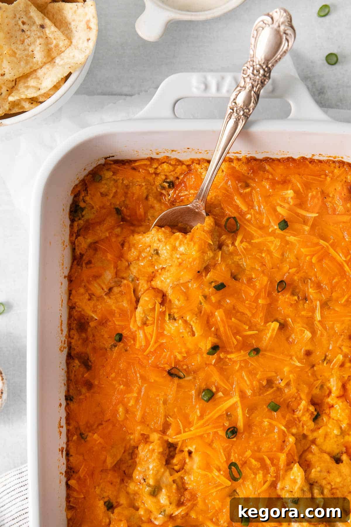 A spoon scooping a generous portion of warm, bubbly dairy-free buffalo chicken dip from a baking dish, highlighting its creamy texture and enticing color, ready to be enjoyed.