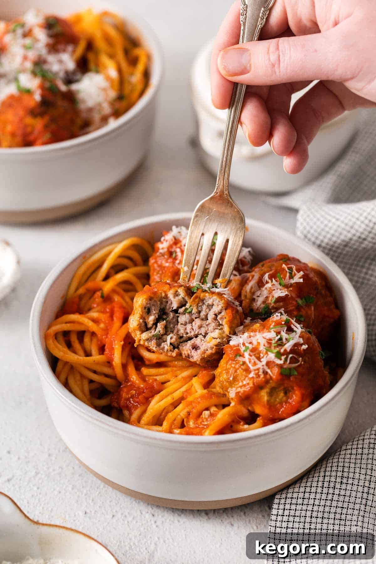 Traditional Italian Gluten Free Meatballs 7 A hand using a fork to pick up a meatball and spaghetti.