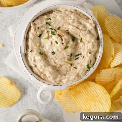 Ultimate Caramelized Onion Dip 10 A top-down view of a creamy homemade caramelized onion dip in a serving bowl, elegantly surrounded by an assortment of various crispy potato chips and garnished with a sprig of fresh chives for visual appeal.