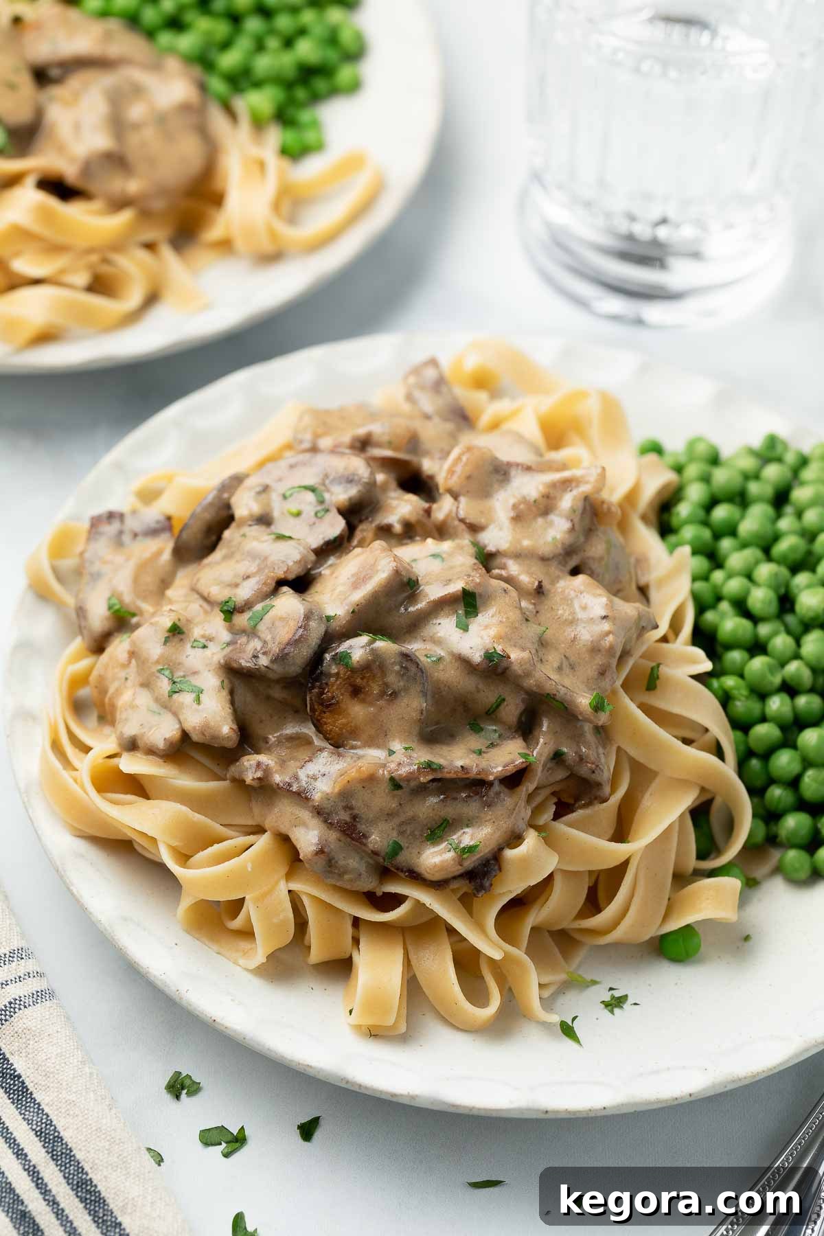 The Truth About Egg Noodles and Gluten 4 beef stroganoff on white plate topped with parsley and served with peas