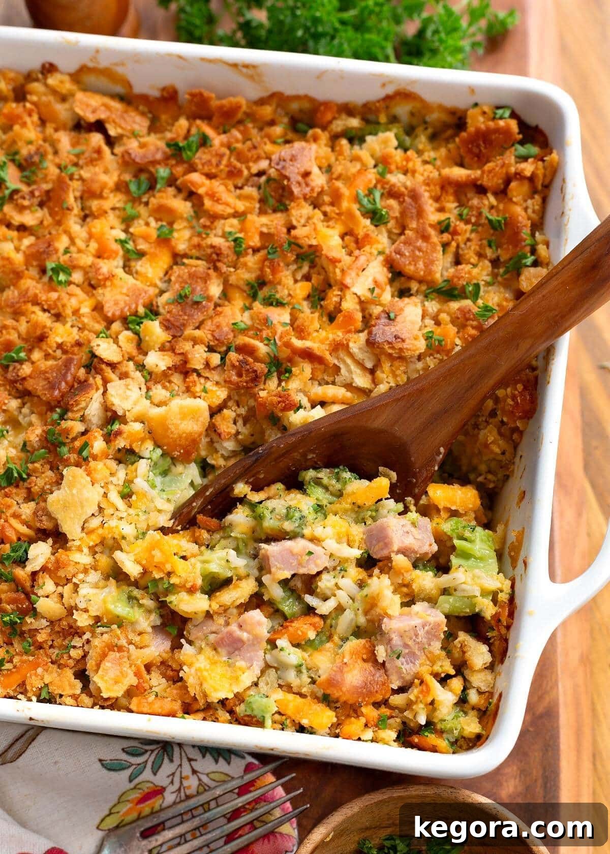 Hearty Ham and Broccoli Rice Bake 2 Close-up of a delicious Ham and Broccoli Rice Casserole with a wooden spoon scooping a portion, highlighting the golden-brown topping and creamy interior.