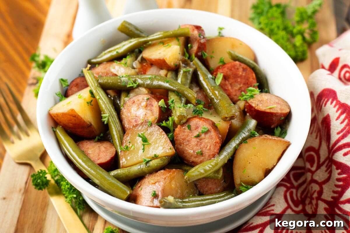 Close-up of cooked Crockpot Swamp Potatoes, showing tender potatoes, sliced sausage, and vibrant green beans in a rich, savory broth.