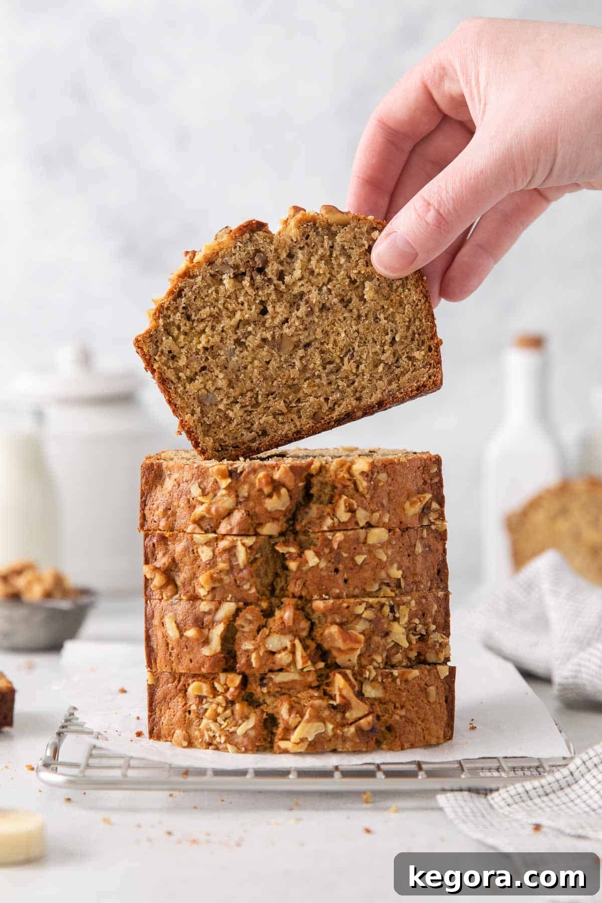 Wholesome Oat Banana Loaf 9 A hand picking up a slice of moist oat flour banana bread from a rustic wooden board.