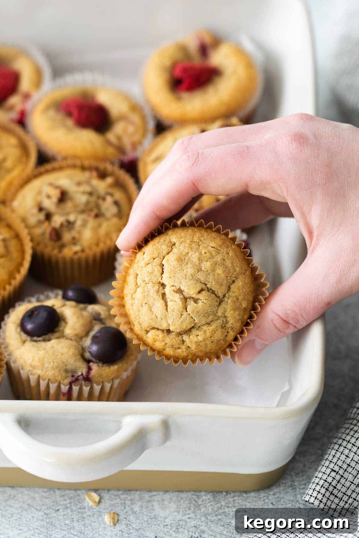 Wholesome Oat Muffins Infinite Variations 9 A hand reaching for a perfectly golden oat flour muffin in a baking dish, highlighting its appeal.