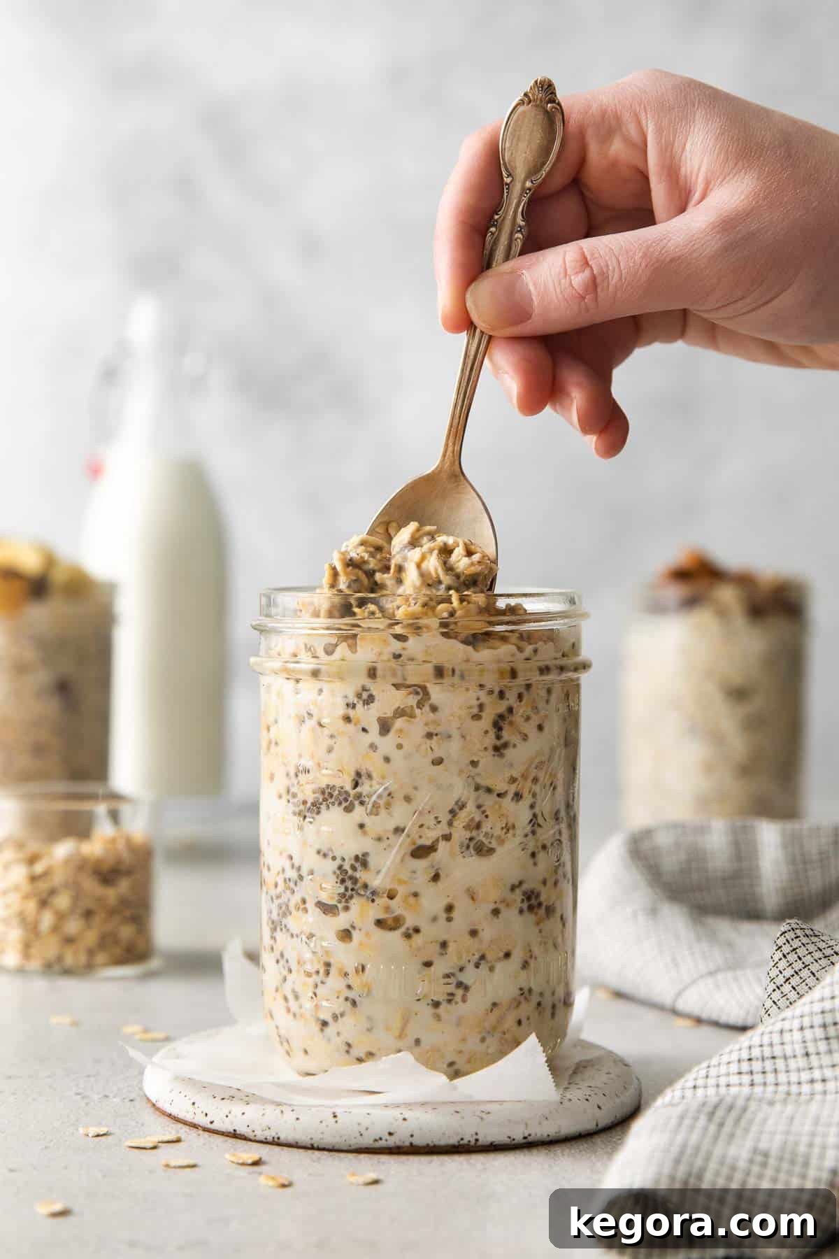 A side view of gluten-free overnight oats in a mason jar, with a hand sticking a spoon in the top, ready to eat.