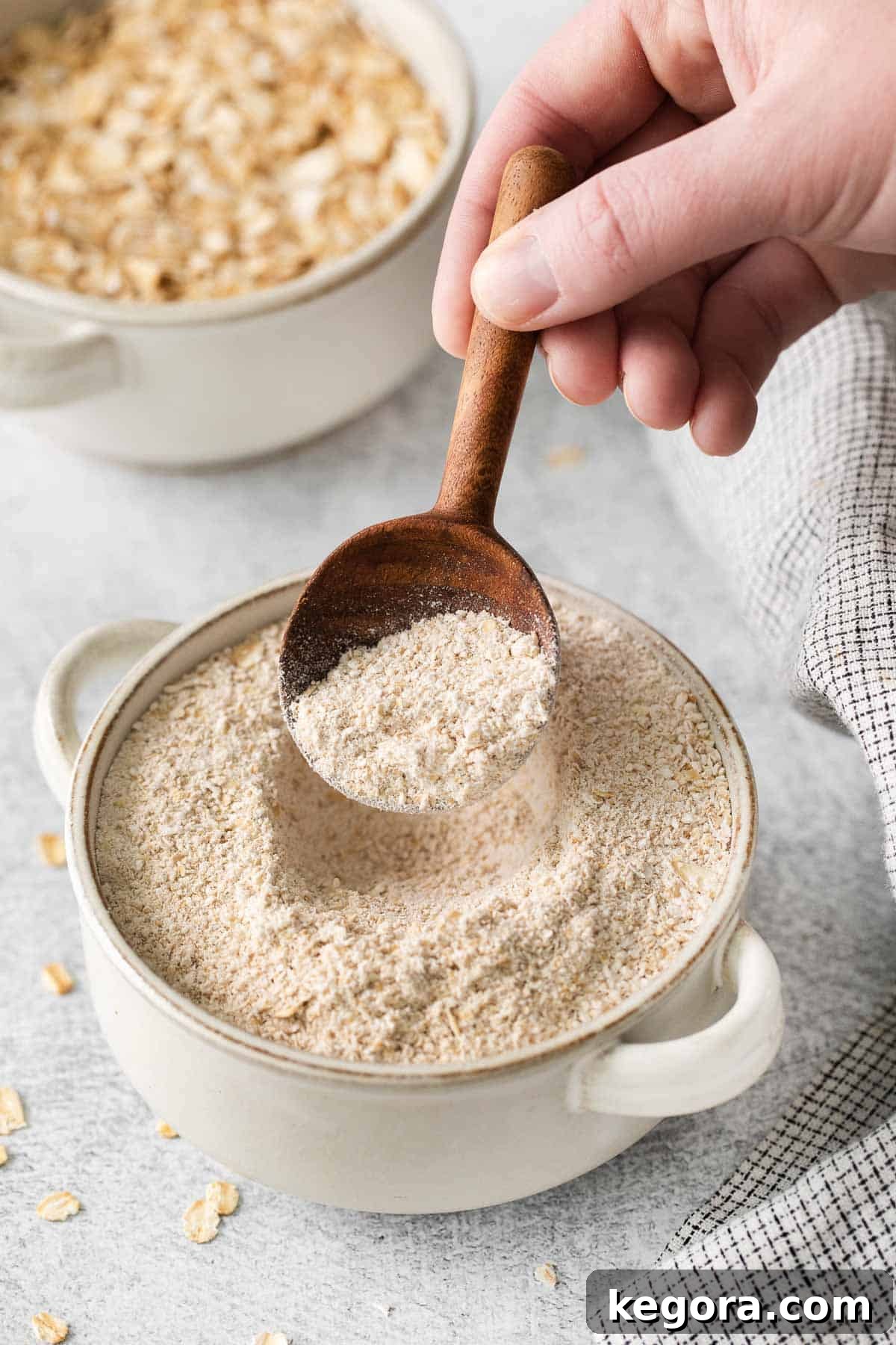 A hand holding a spoon and scooping up gluten-free oat flour from a bowl