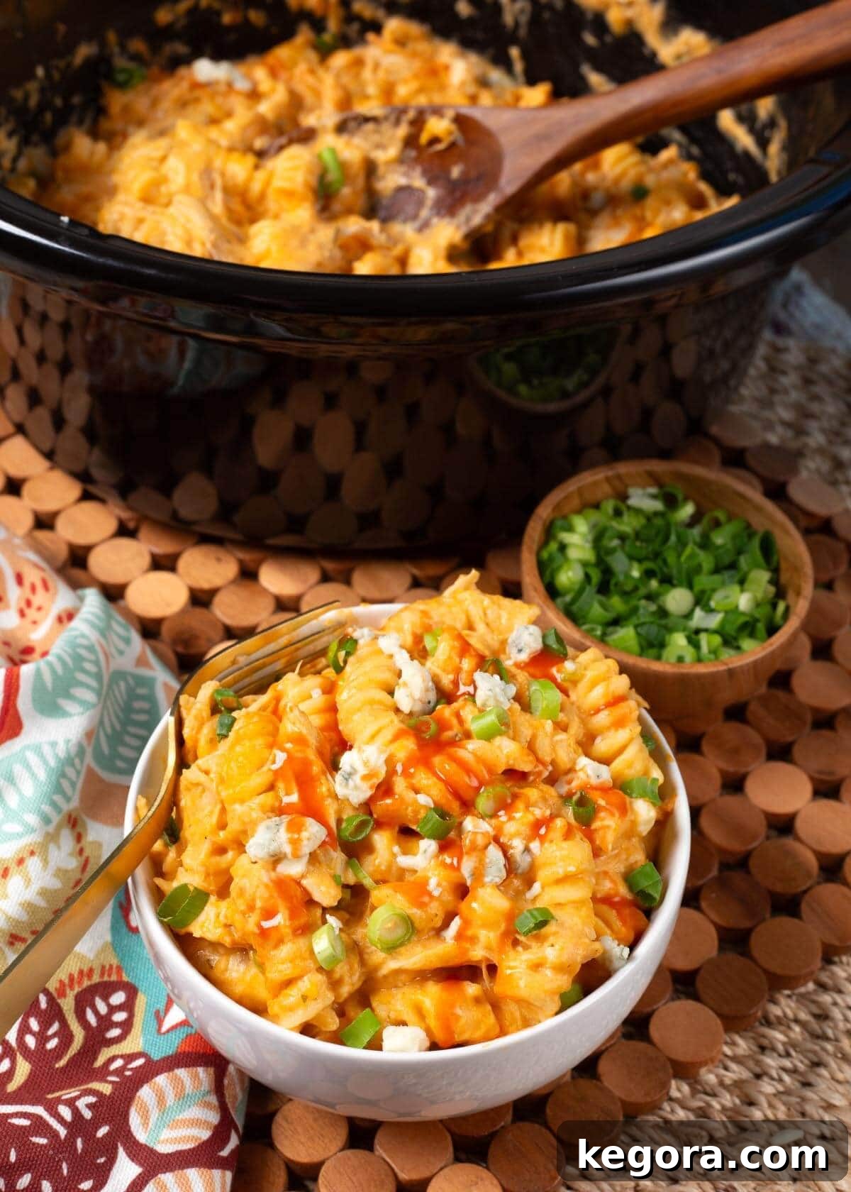 Overhead shot of a full slow cooker of Crockpot Buffalo Chicken Mac and Cheese, garnished with green onions and blue cheese