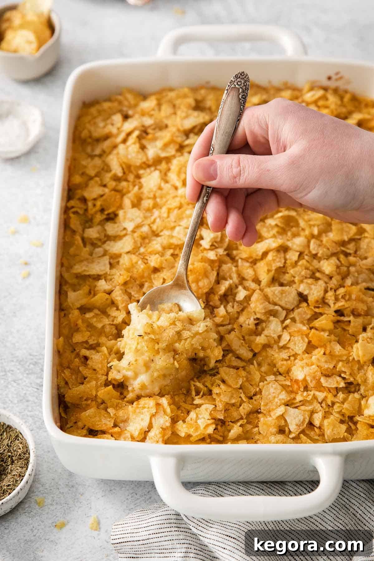 Ultimate Gluten-Free Cheesy Potato Bake 3 Golden brown gluten-free cheesy potatoes in a baking dish, ready to be served, with a serving spoon.