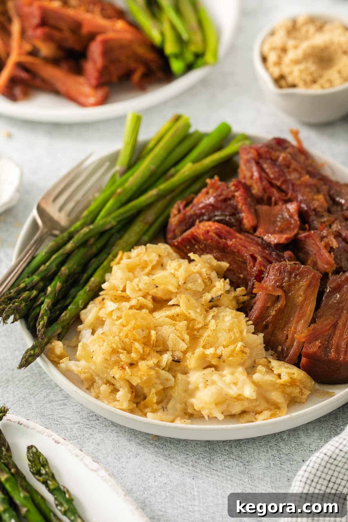 Ultimate Gluten-Free Cheesy Potato Bake 9 A plate of gluten-free cheesy potatoes served alongside sliced ham and fresh asparagus.