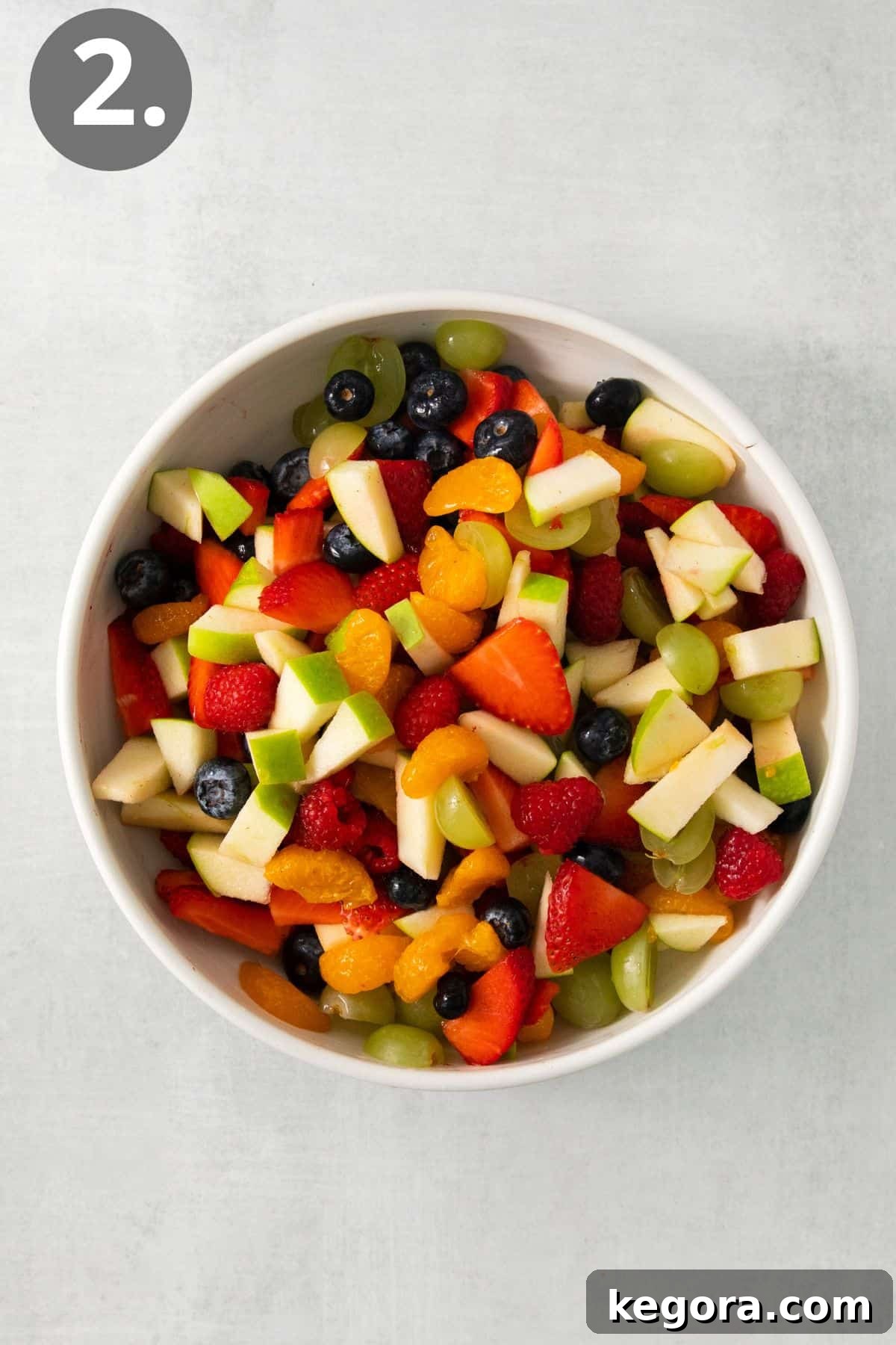 Festive Easter Fruit Delight 6 A bowl of mixed chopped fruit, including red berries, green grapes, and yellow mandarin oranges, coated with a light liquid.
