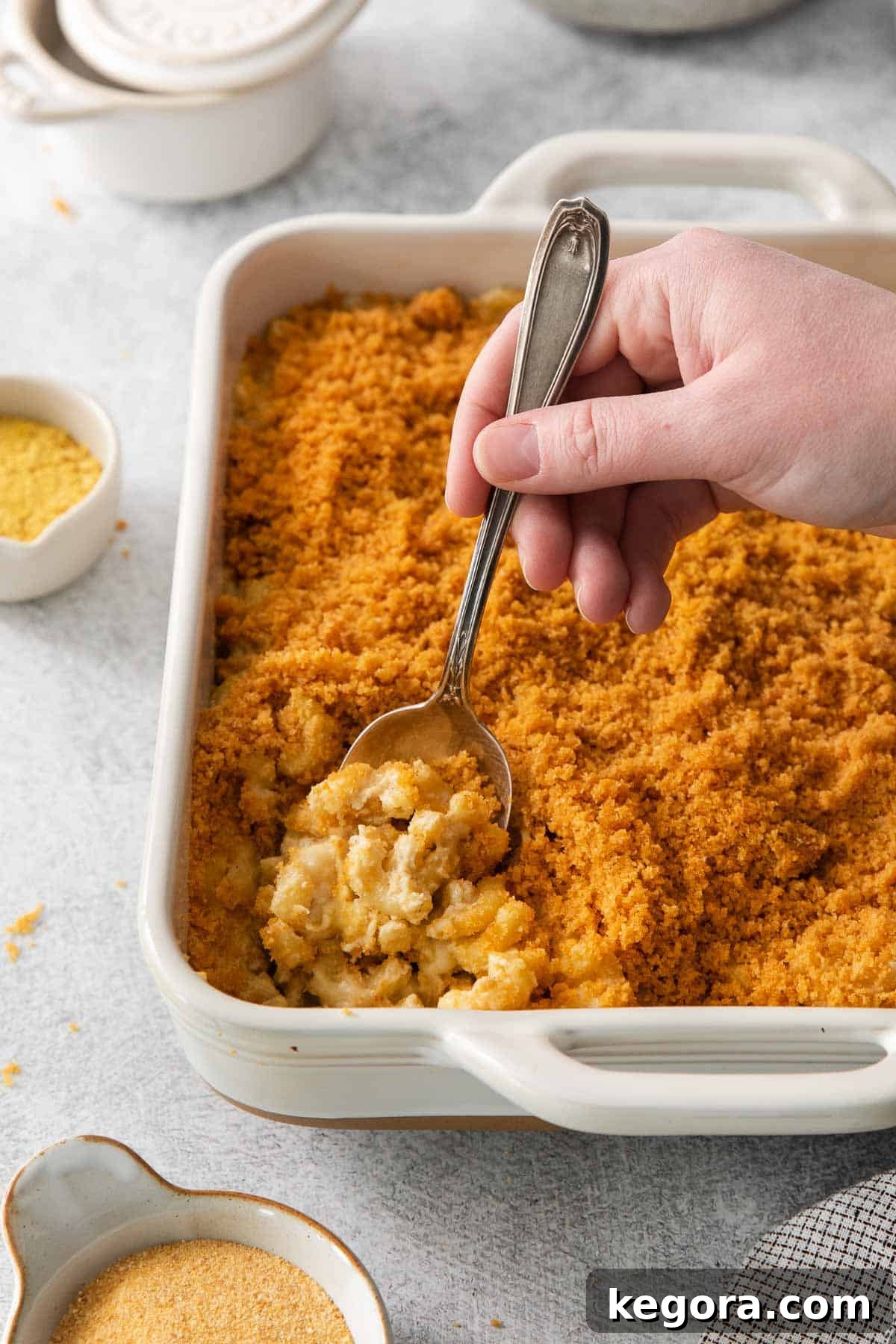 Vegan Mac and Cheese 10 A hand scooping a generous portion of creamy dairy-free mac and cheese out of a baking dish, highlighting its rich texture.