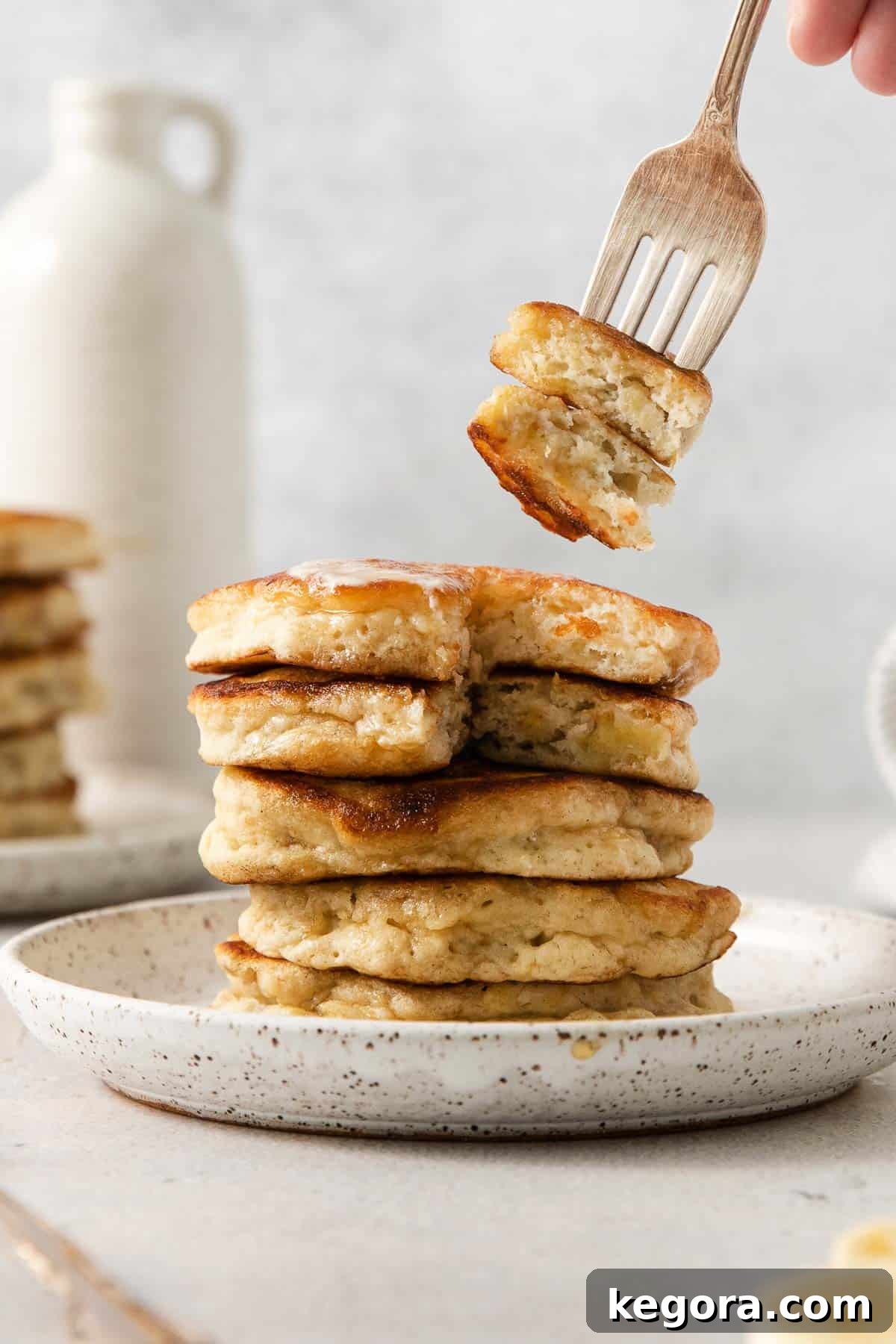 Naturally Sweet Gluten-Free Banana Hotcakes 10 Gluten-free banana pancakes stacked on a plate with a fork taking a bite out of them, showcasing their fluffy interior.