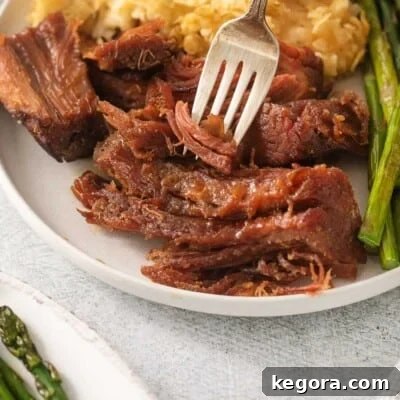 A generous slice of tender, glazed gluten-free ham on a white plate, with a fork poised to take a bite, highlighting its savory goodness.
