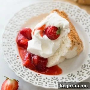 A slice of light and airy gluten-free angel food cake on a white plate with fresh strawberries.