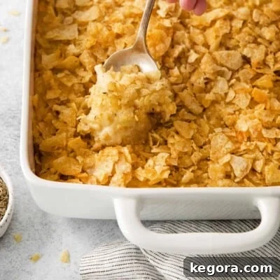 A close-up of golden-brown gluten-free cheesy potatoes in a baking dish, featuring a serving spoon ready to scoop, highlighting their creamy texture and crispy topping.