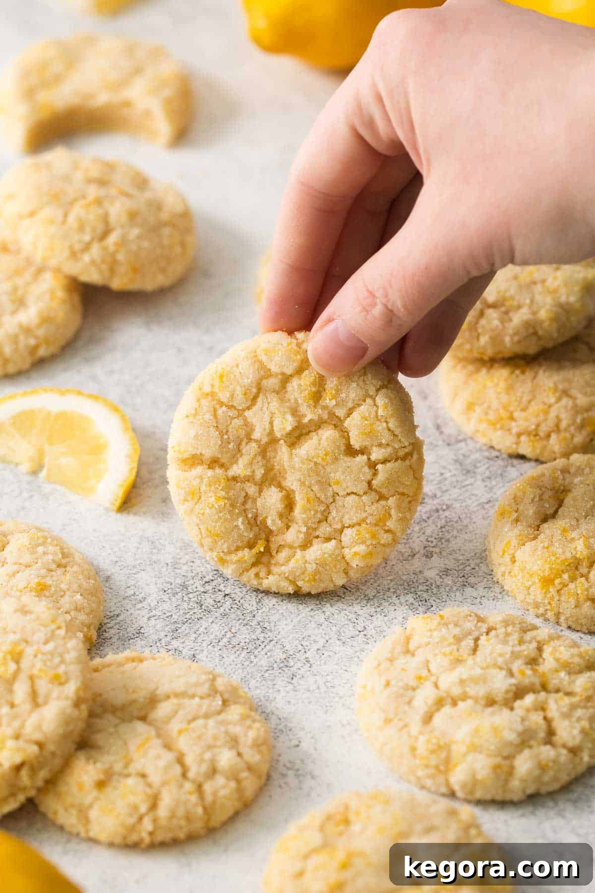 Zesty Lemon Gluten-Free Delights 13 Lemon cookies on parchment paper with a wedge of lemon and a hand picking up a cookie