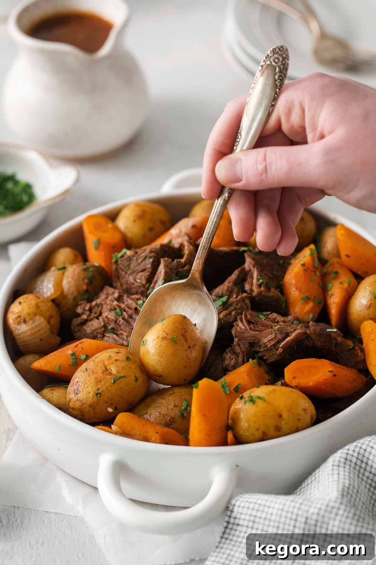 Spoon lifting a piece of sirloin roast with carrots and potatoes, showing tenderness