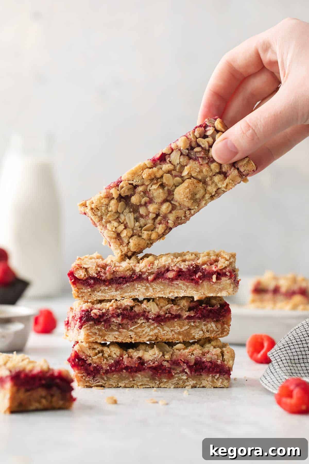 Flourless Raspberry Streusel Squares 4 Gluten-free raspberry bars stacked on top of each other and a hand picking up the top bar