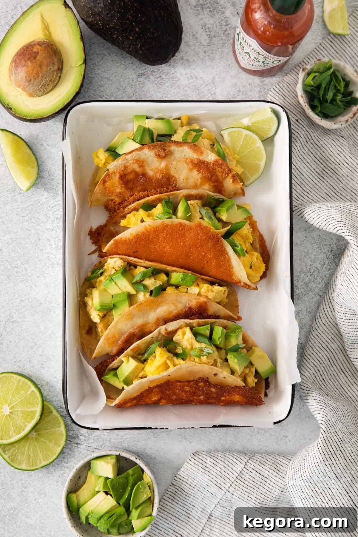 An overhead view of vibrant breakfast tacos nestled in a baking dish lined with parchment paper, showcasing their delicious toppings and golden-brown tortillas.