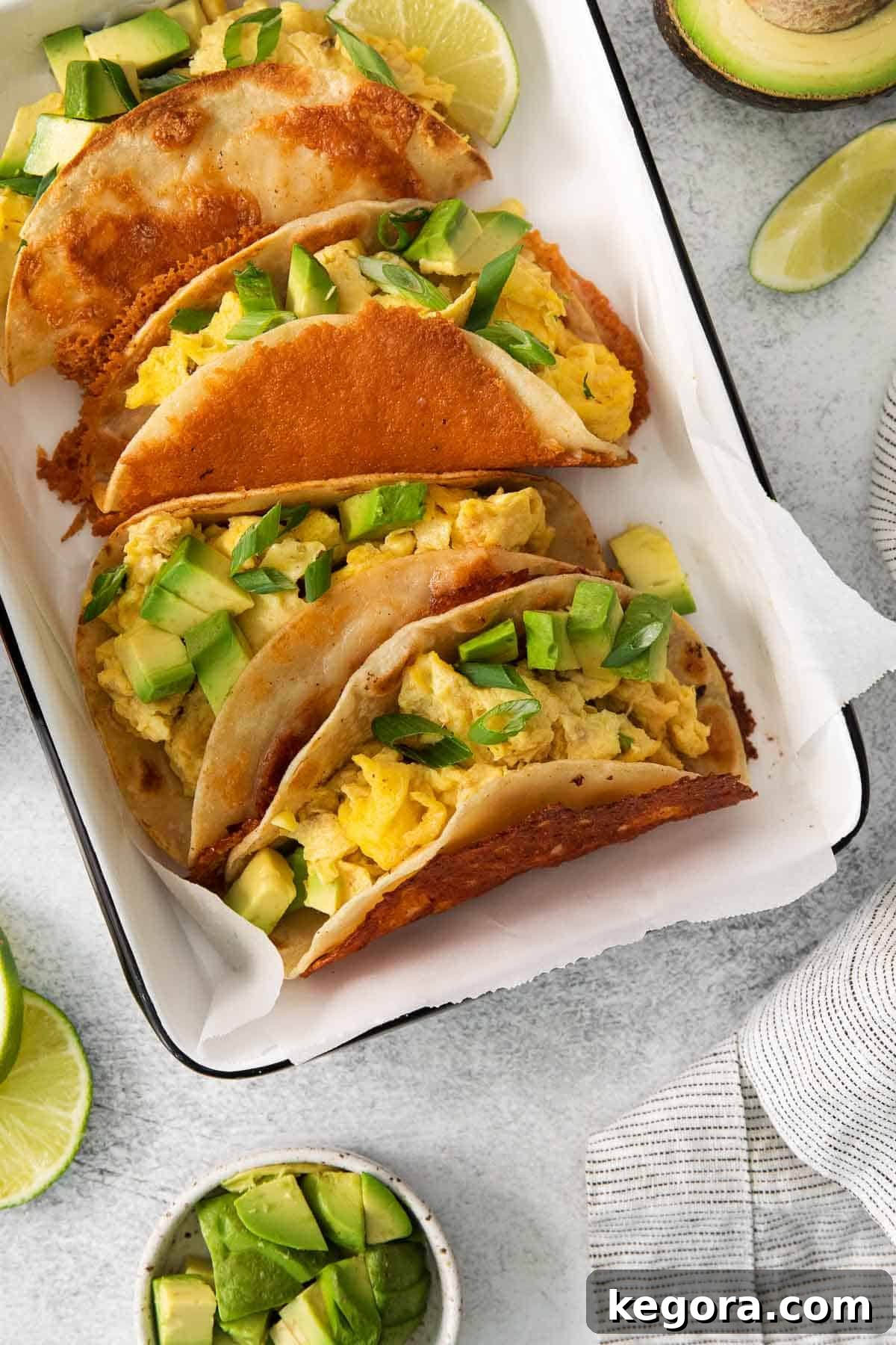 A close-up shot of perfectly prepared breakfast tacos arranged in a baking dish lined with parchment paper, showcasing their appealing presentation.