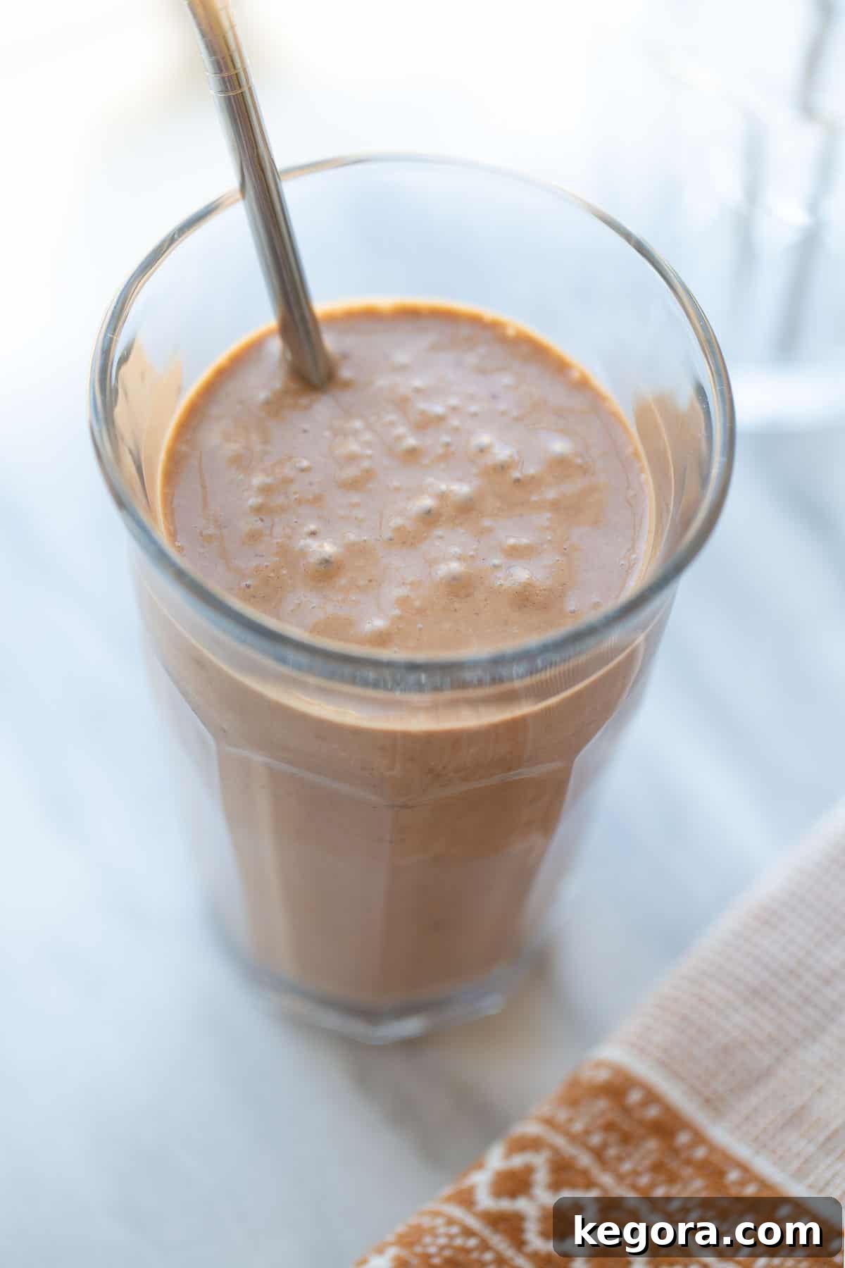 healthy chocolate shake with peanut butter and banana A healthy and rich chocolate peanut butter banana smoothie served in a clear glass with a sustainable metal straw, ready to be enjoyed.
