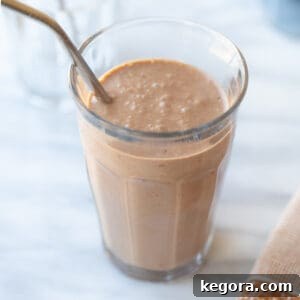 A glass of creamy peanut butter banana smoothie with a metal straw, inviting a refreshing sip.