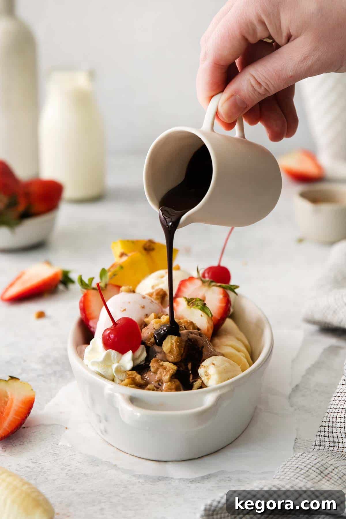 Timeless Banana Split Indulgence 2 A banana split on a table with a hand pouring chocolate syrup on top