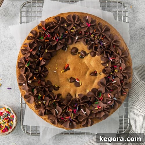 An overhead view of a festive gluten-free cookie cake with chocolate frosting and sprinkles on a wire rack.