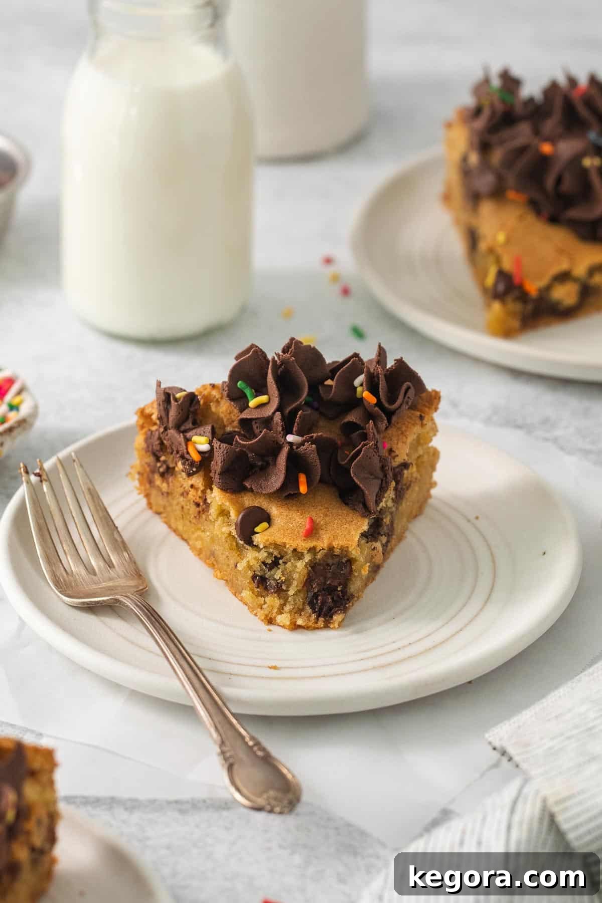 Irresistible Gluten-Free Cookie Cake 10 A slice of gluten-free cookie cake on a white plate with a fork, accompanied by a glass of milk in the background, inviting indulgence.