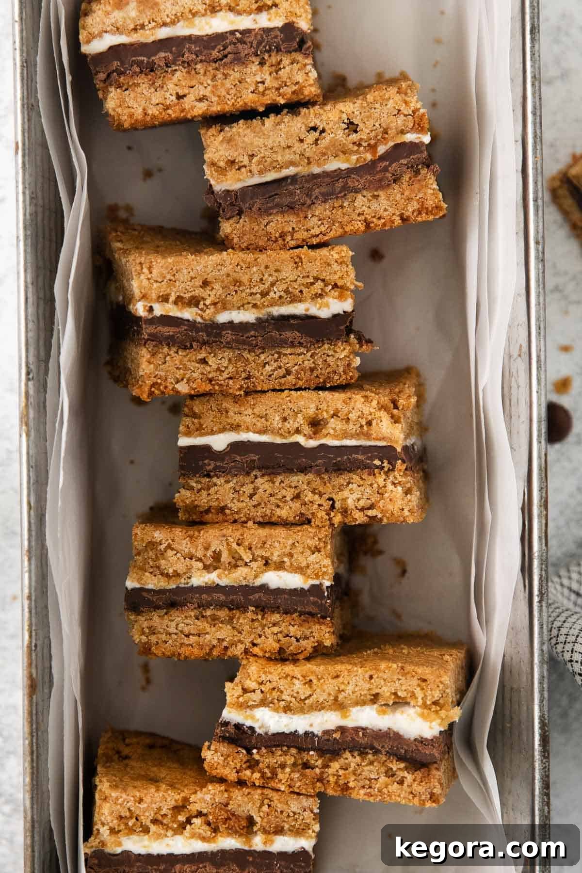 Perfectly sliced gluten-free s'mores bars with visible layers of cookie, chocolate, and marshmallow, arranged on their sides in a baking pan.