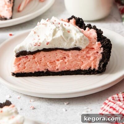 A close-up view of a slice of gluten-free peppermint Oreo pie on a plate, showcasing the distinct layers and festive garnishes.