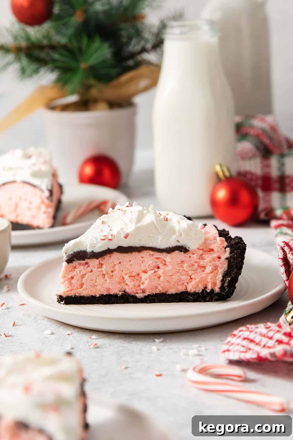 Gluten-Free Minty Oreo Delight 9 A beautiful side view of a slice of gluten-free peppermint Oreo pie on a white plate, showcasing the distinct layers of crust, pink filling, ganache, and whipped cream.