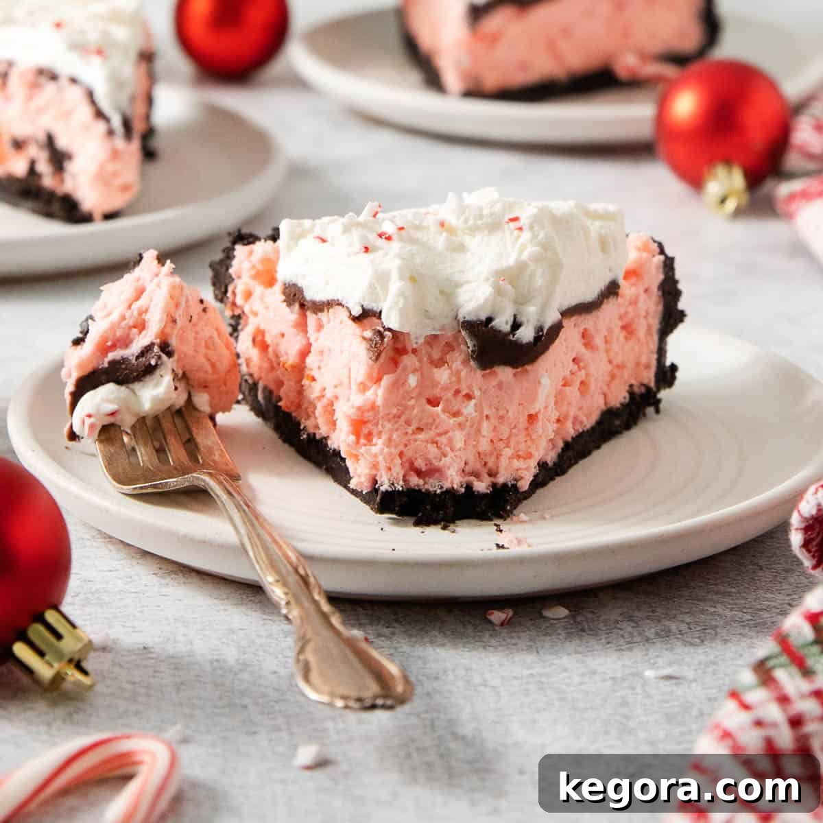 Gluten-Free Minty Oreo Delight 10 A slice of gluten-free peppermint Oreo pie on a white plate, with a fork poised to take a bite, highlighting its tempting layers of crust, pink filling, and whipped topping.
