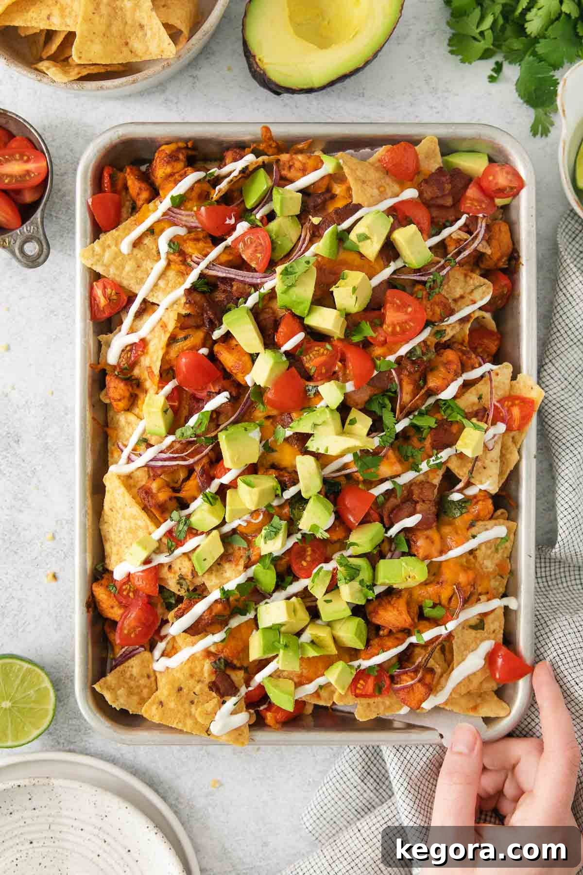 Ultimate BBQ Chicken Nachos 3 BBQ chicken nachos on a sheet pan with a hand reaching for a portion, highlighting their irresistible appeal.