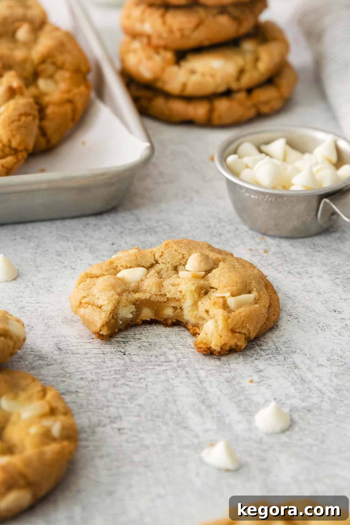 A freshly baked gluten-free white chocolate macadamia nut cookie with a bite taken out of it, showing its soft, chewy interior, resting on a baking tray.