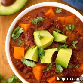 Sweet potato chili in a white bowl on wooden board garnished with chopped avocados