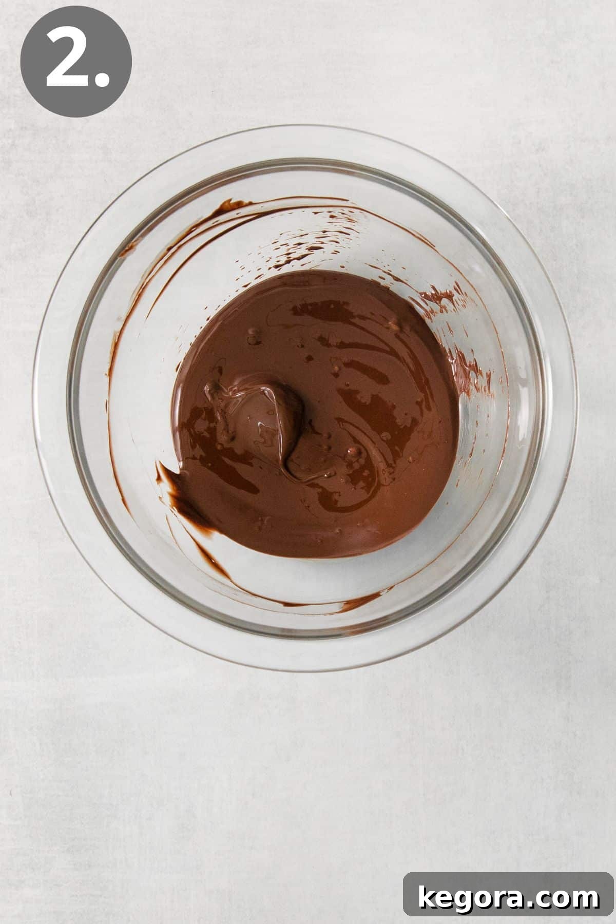 SnickerPop Crunch 5 A clear glass bowl filled with smoothly melted semi-sweet chocolate chips, showing a rich, glossy consistency, ready for drizzling.