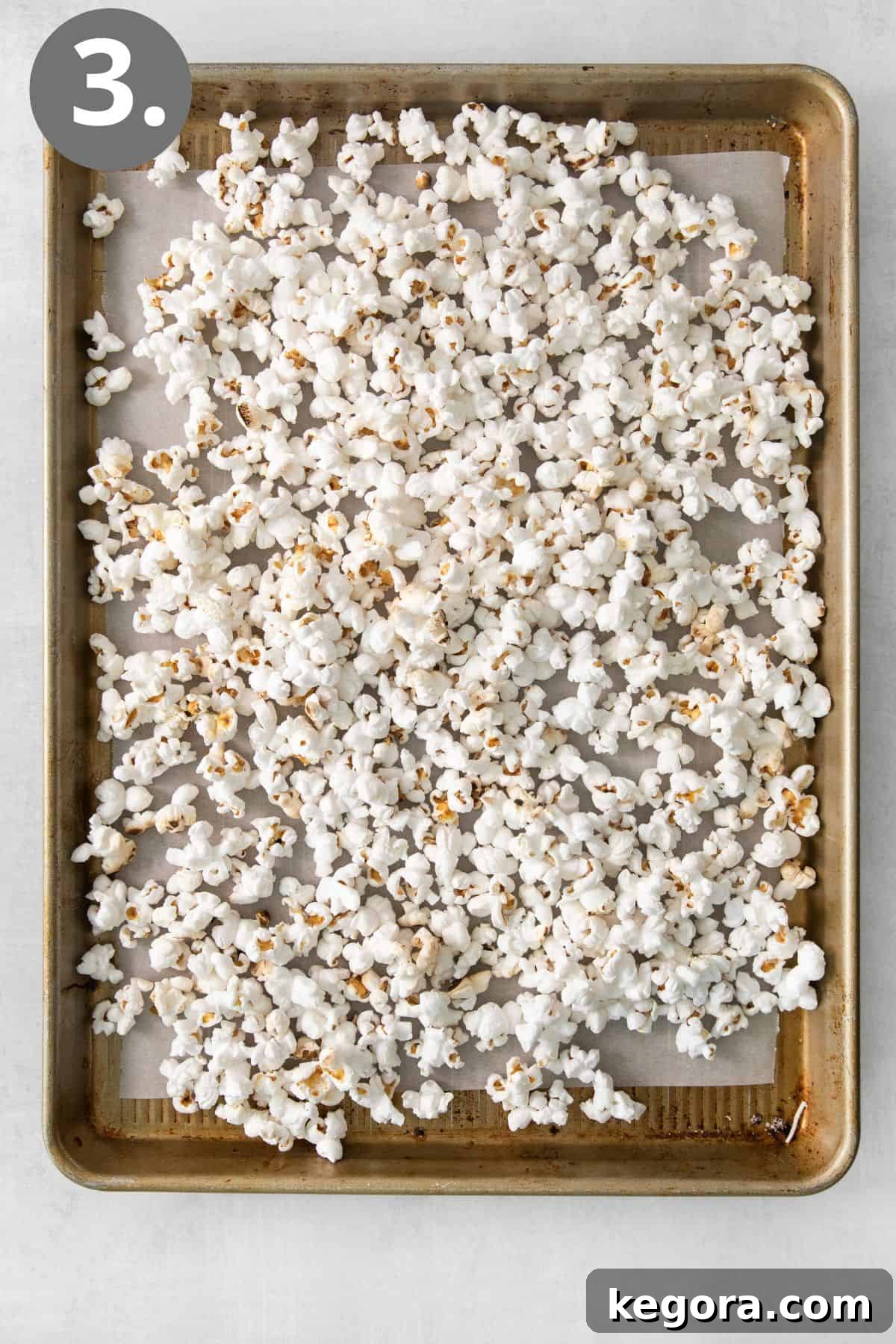 SnickerPop Crunch 6 Freshly popped white popcorn spread evenly in a single layer on a large, rimmed baking sheet, prepared for the next step of topping.