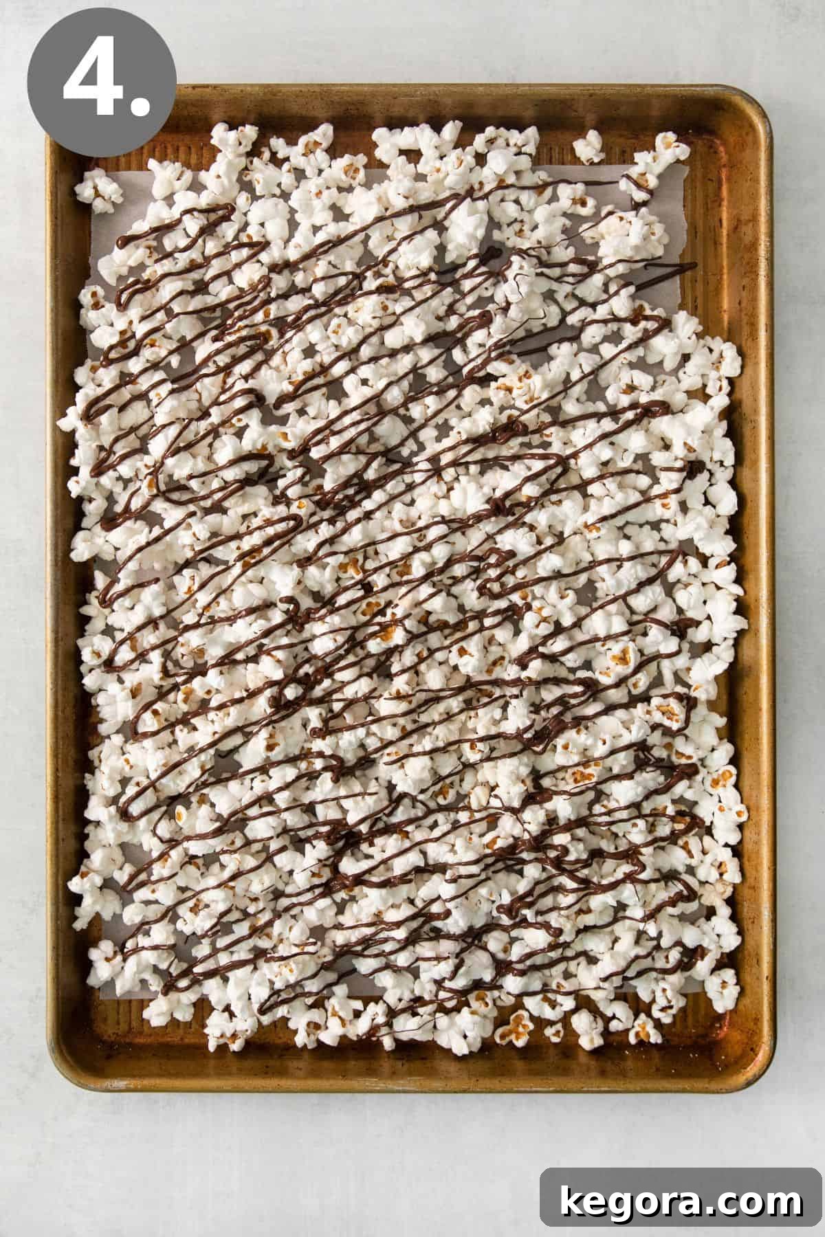 SnickerPop Crunch 7 Popcorn kernels on a baking tray, generously drizzled with melted dark chocolate, ready for the next additions.