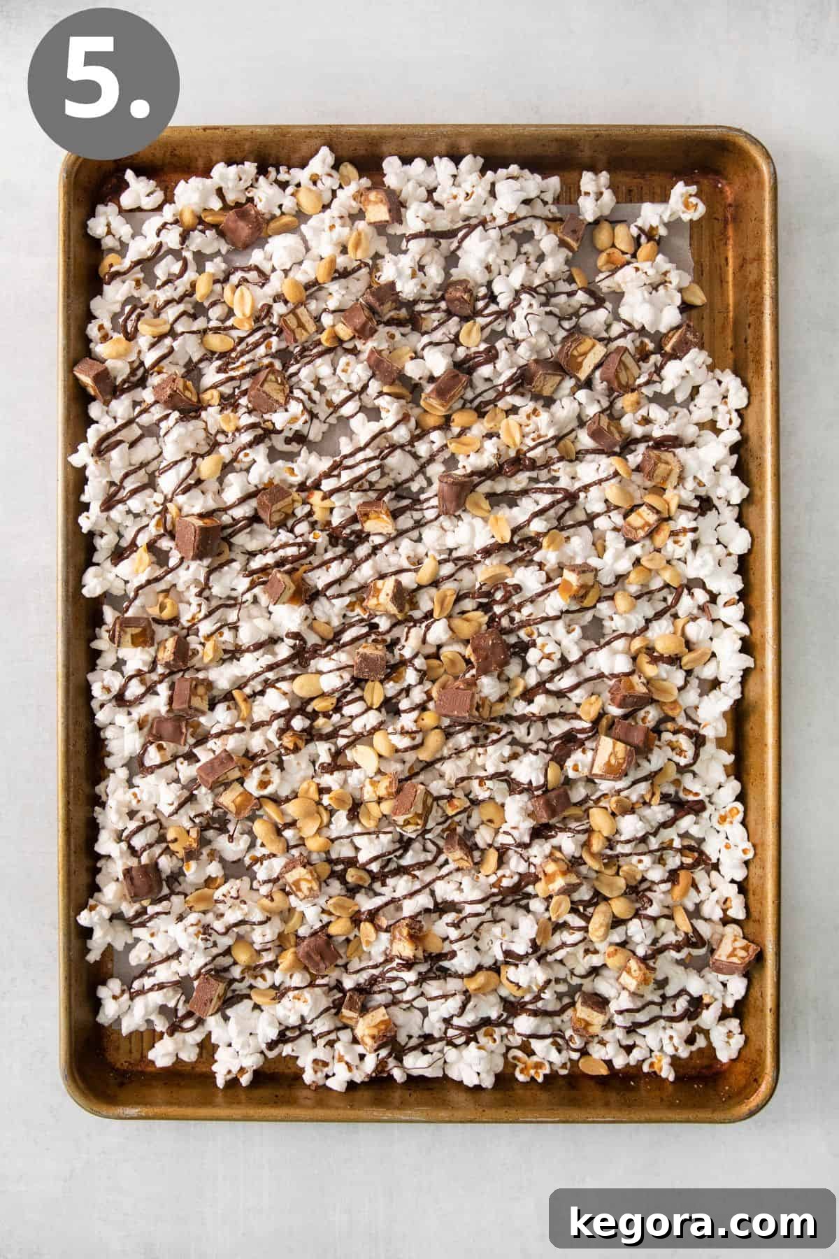 SnickerPop Crunch 8 A baking tray of popcorn, beautifully drizzled with chocolate, and generously sprinkled with chopped Snickers bars and whole roasted peanuts, creating a visually appealing snack.